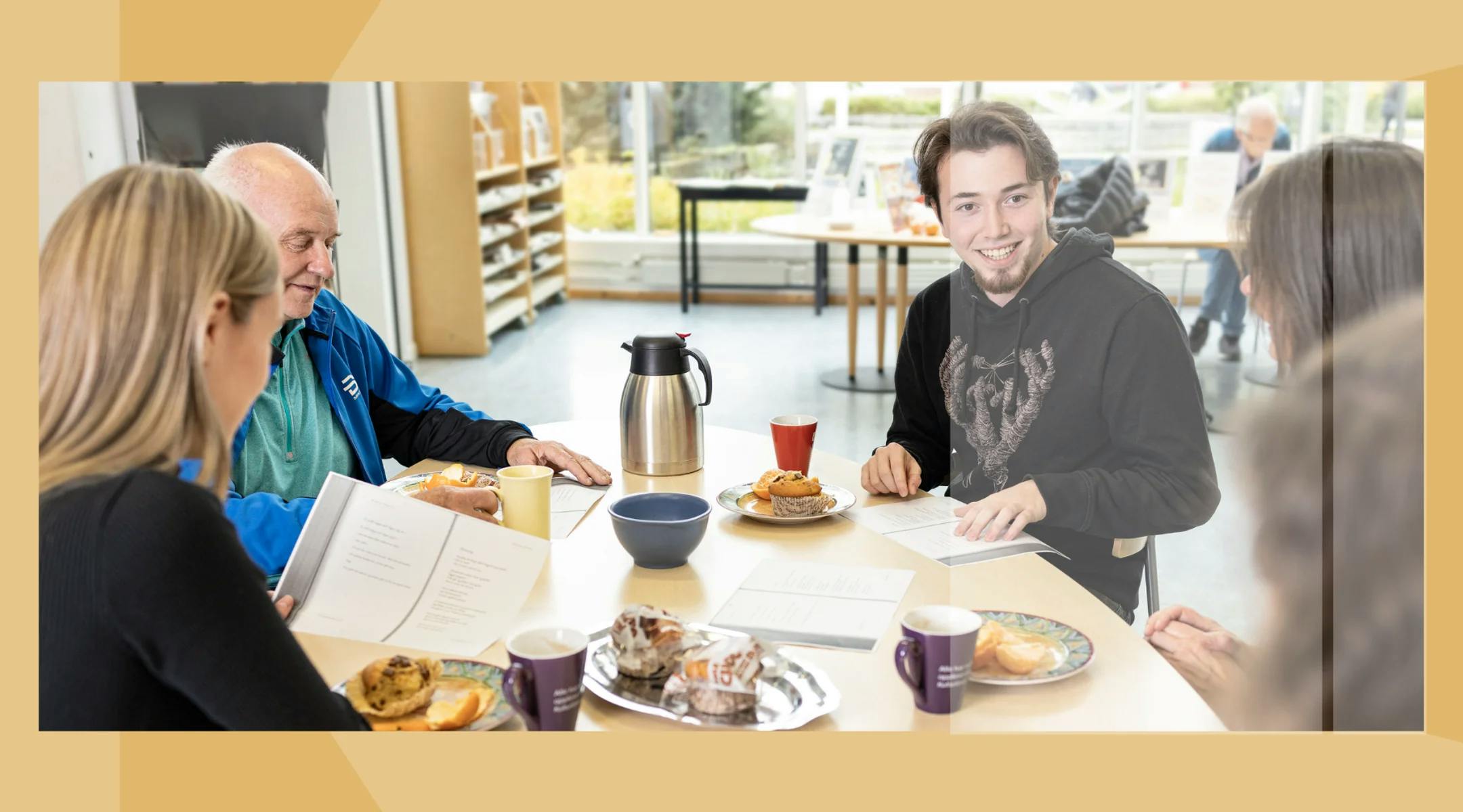 Fem personer sitter rundt et bord. På bordet er det ark, kaffe, muffins og appelsin.